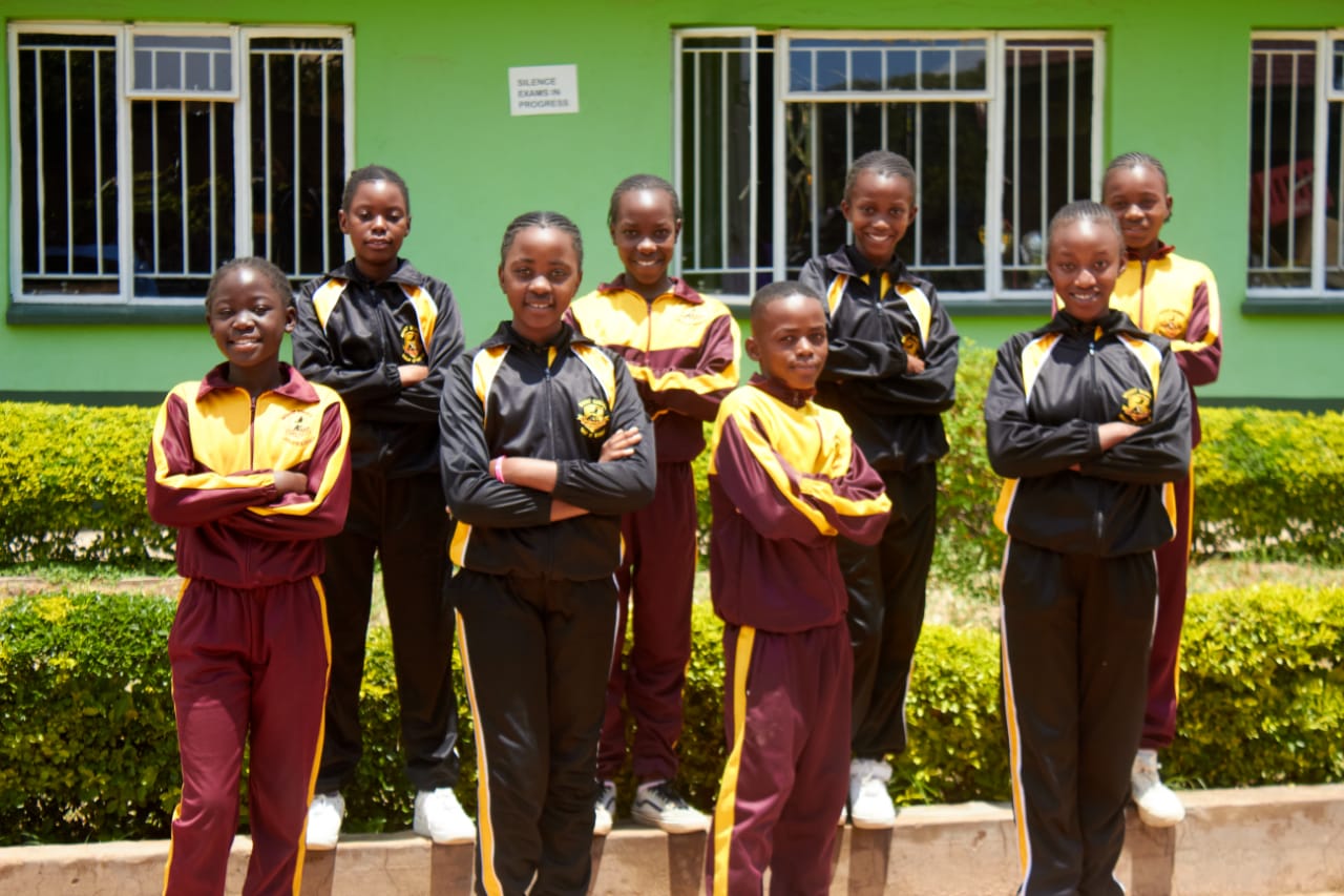 Learners in maroon and gold tracksuits in front of a classroom block
