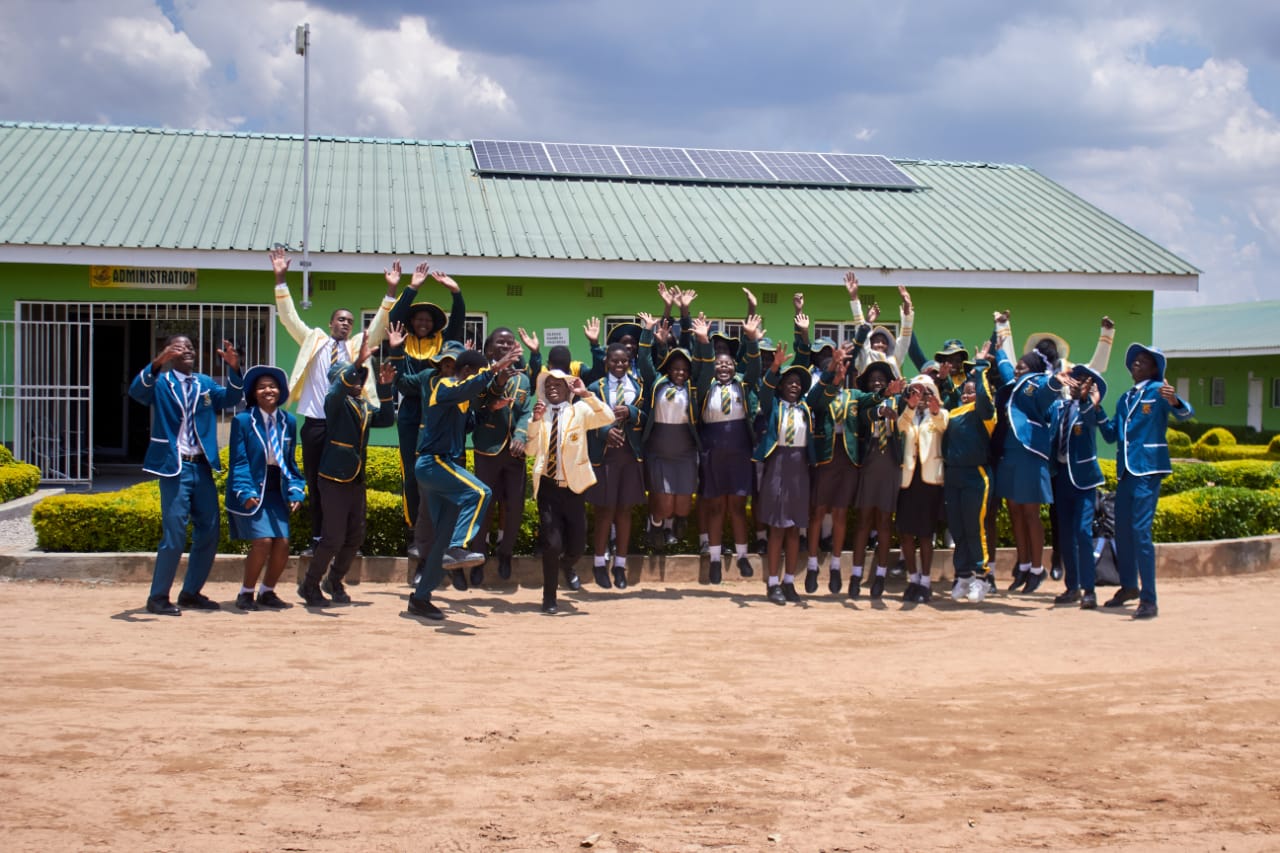 Learners cheering in front of a classroom block